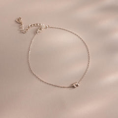 Close up of a dainty silver bubble letter M bracelet against a neutral background.