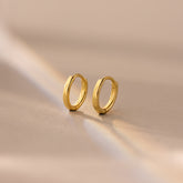 Pair of 8mm gold small dainty huggie hoop earrings resting on a soft beige surface.