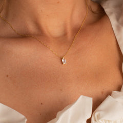 Gold necklace featuring a rectangular emerald-cut crystal pendant, worn by a model in a white ruffled top, highlighting the clean, geometric lines and radiant clarity of the stone.