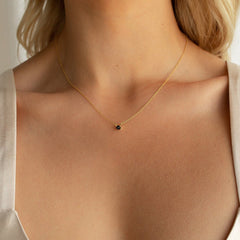 Model wears a minimalist gold chain necklace featuring a small round black onyx stone set in a dainty prong setting at the center of the collarbone.