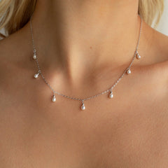Dainty silver chain necklace adorned with evenly spaced small white pearl drops, worn by a model with a bare neckline.