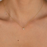 Gold chain necklace with a small butterfly-shaped pendant adorned with clear gemstones, worn with a strapless nude top.