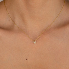 Gold chain necklace with a small butterfly-shaped pendant adorned with clear gemstones, worn with a strapless nude top.