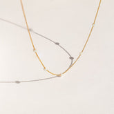 Delicate gold chain necklace with evenly spaced small opal beads, shown casting soft shadows on a light cream background.