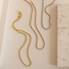 Gold, rose gold, and silver rope chain necklaces laid out side by side on a light surface.