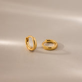 Pair of 6mm tiny dainty gold huggie hoop earrings displayed on a neutral satin surface with soft lighting.