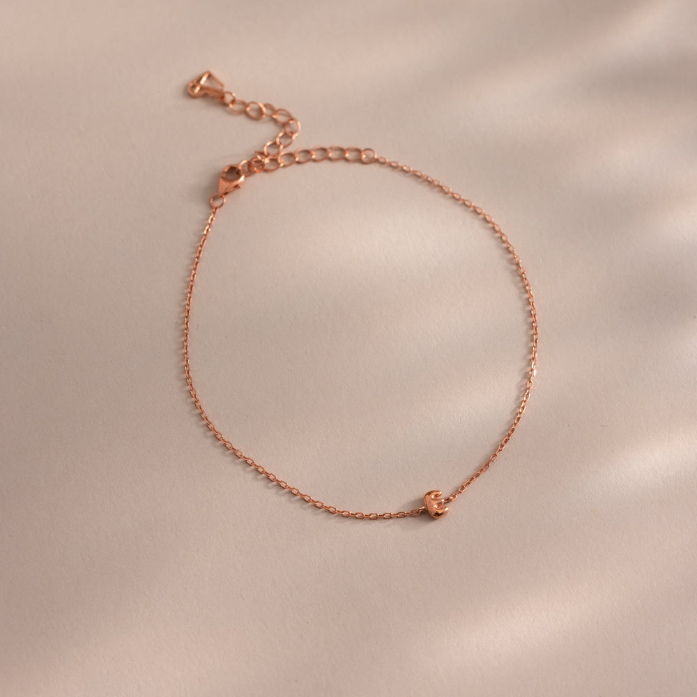 Close up of a dainty rose gold bubble letter E bracelet against a neutral background.